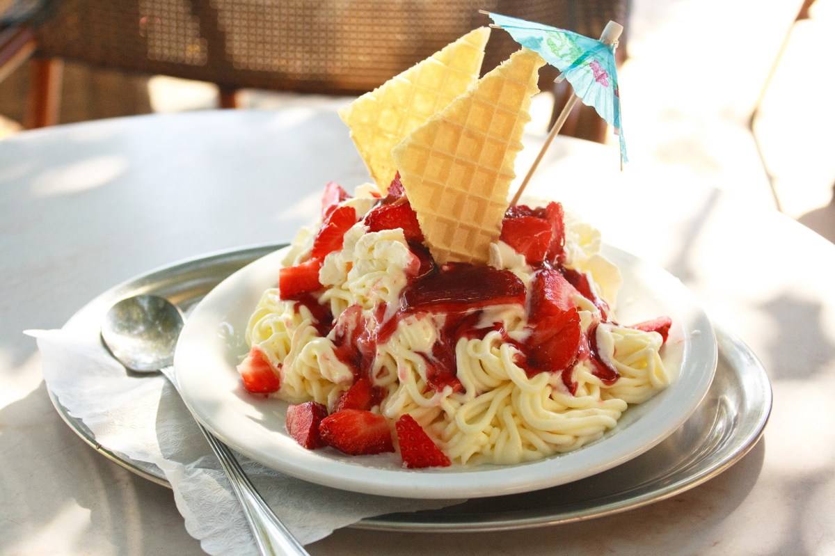 Spaghetti-Eis selber machen: Spaghetti-Eis angerichtet auf einem weißen Teller, garniert mit frischen Erdbeeren und Eiswaffeln.
