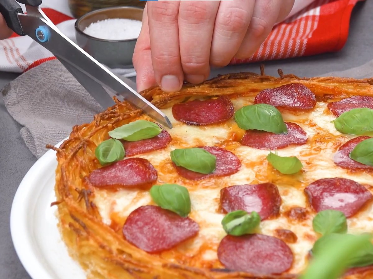 Spaghetti-Bolognese-Pizza wird mit Schere geschnitten.