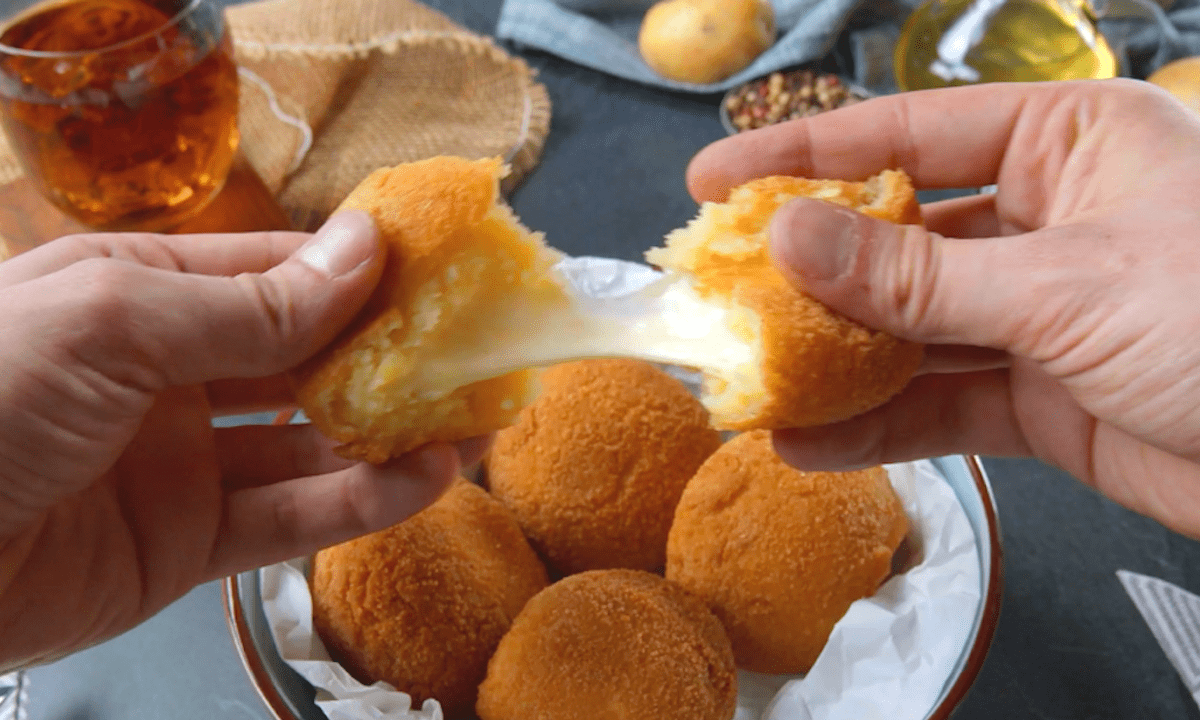 Ein Kartoffel-Käse-Bällchen über weiteren Bällchen auf einem Teller wird mit zwei Händen auseinander gezogen