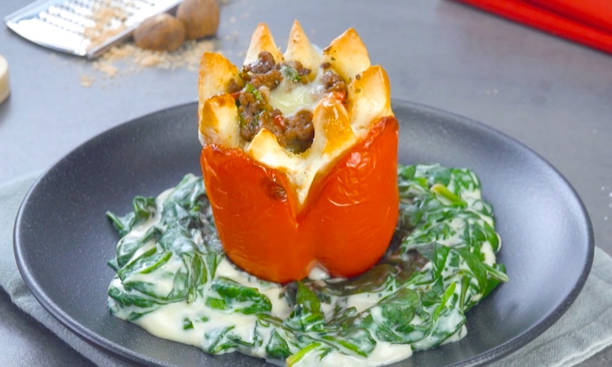 Eine gefÃ¼llte Paprika mit Hackfleisch auf einem Teller, die aussieht wie eine Blume. Dazu gibt es Spinat-Sahne-SoÃŸe.