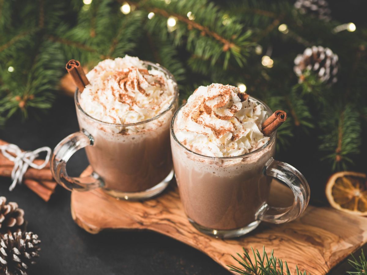 Zwei Becher mit heiÃŸer Schokolade mit Earl Grey stehen auf einem Holzbrett. Weihnachtliche Deko liegt davor und im Hintergrund.