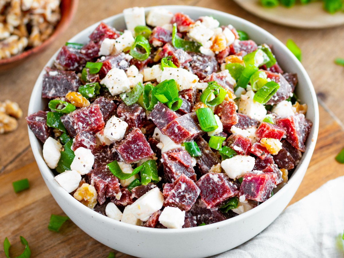 Rote-Bete-Salat mit Schafskäse, Walnusskernen und Frühlingszwiebeln, serviert in einer weißen Schüssel. Im Hintergrund sind Walnüsse und Frühlingszwiebeln zu sehen