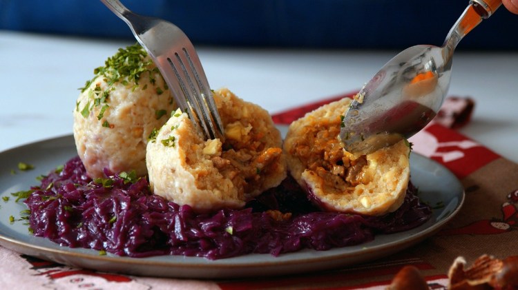 Zwei Maronenknödel mit Entenfüllung auf einem Teller mit Rotkohl. Einer der Knödel wurde aufgeschnitten, um die Füllung zu präsentieren.