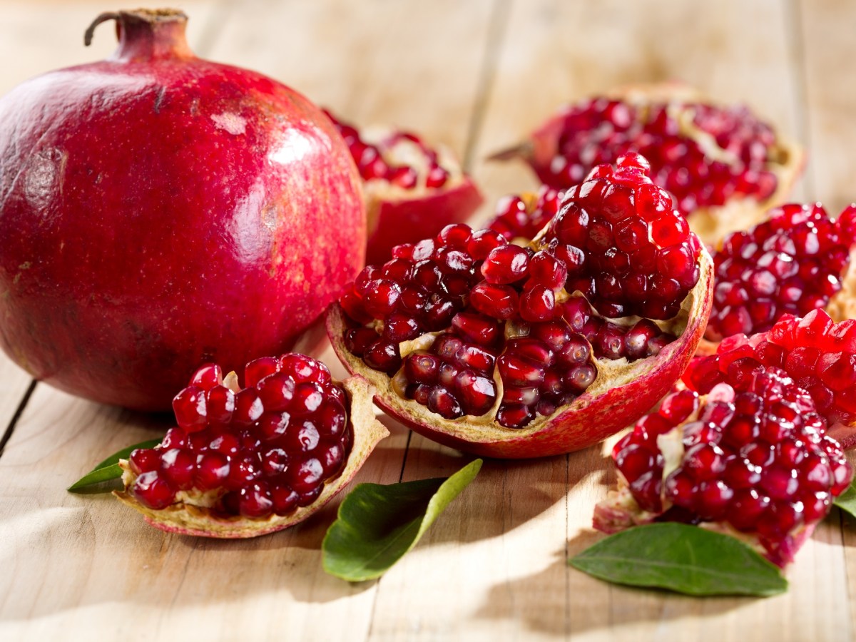 Granatapfel entkernen: ein ganzer und ein geÃ¶ffneter Granatapfel auf Holz.