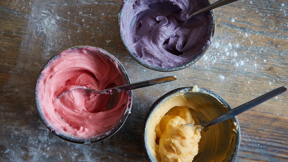 3 Schüssel mit verschieden farbigen Teigen. Einer in lila, einer in rosa und einer in gelb.