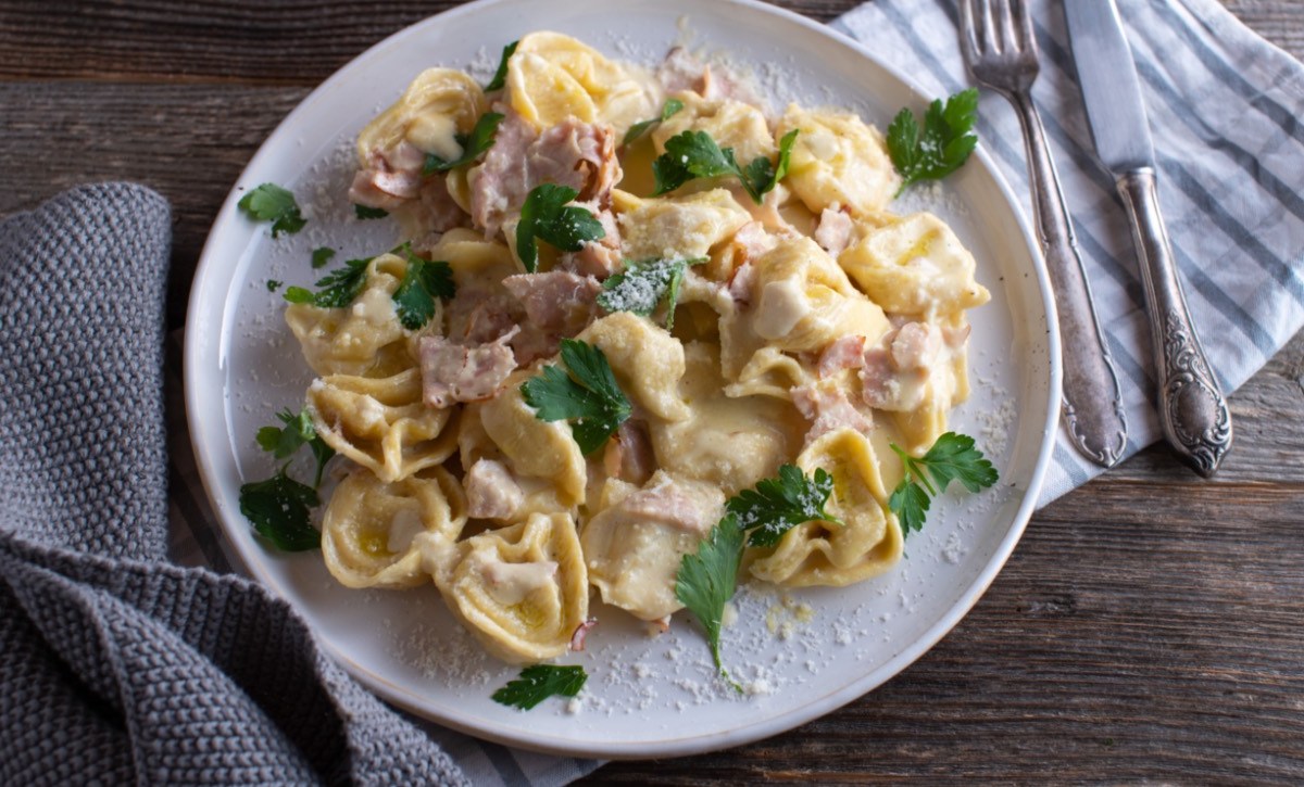 Eine Portion Tortellini alla panna auf einem weißen Teller. Besteck liegt daneben.