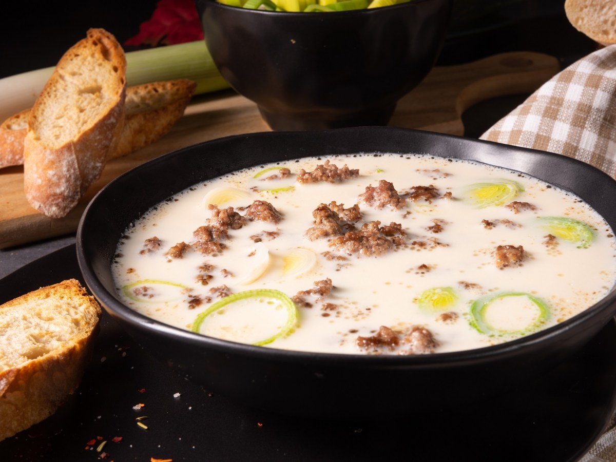 Eine SchÃ¼ssel vegane KÃ¤se-Lauch-Suppe mit Hack, daneben gerÃ¶stete Baguettescheiben.