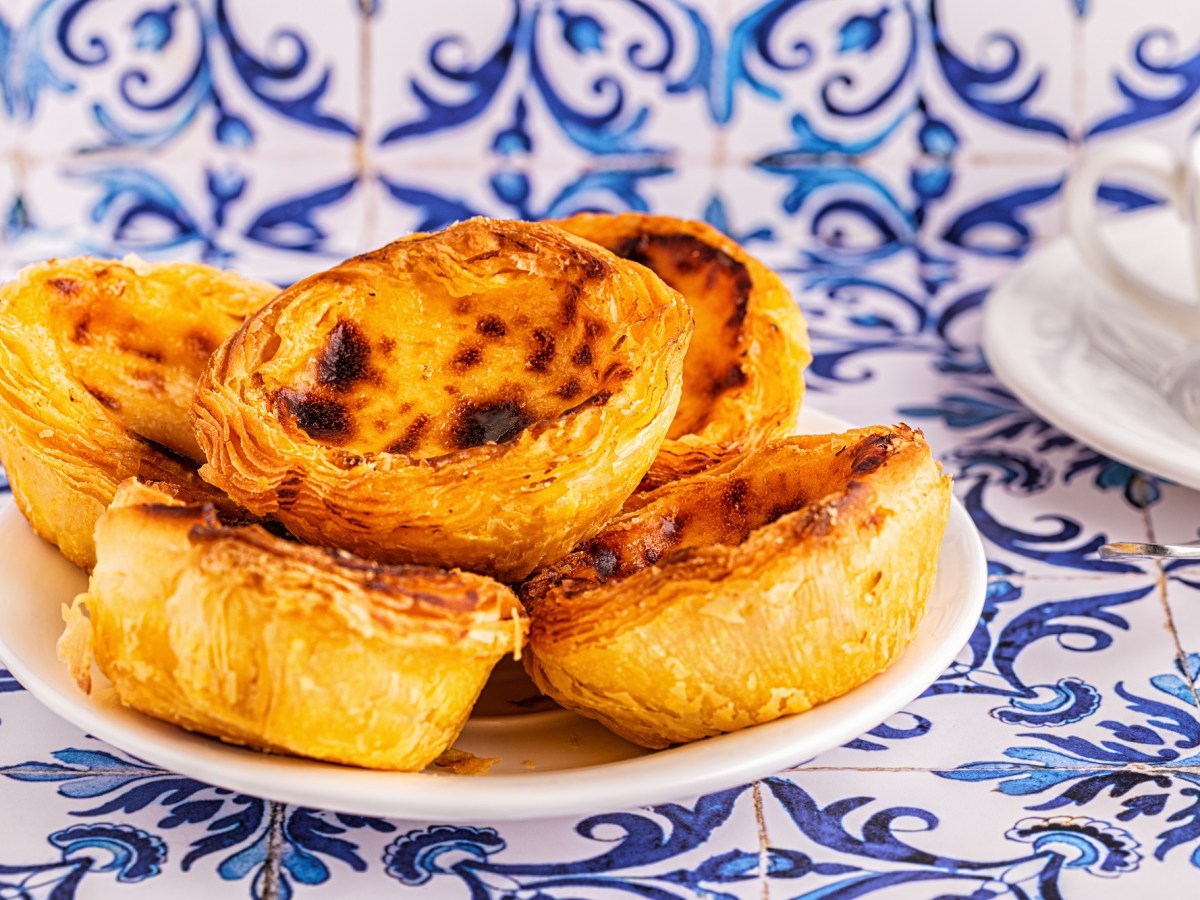 Ein Teller vegane Pastéis de Nata auf typischen blauen portugiesischen Fliesen.