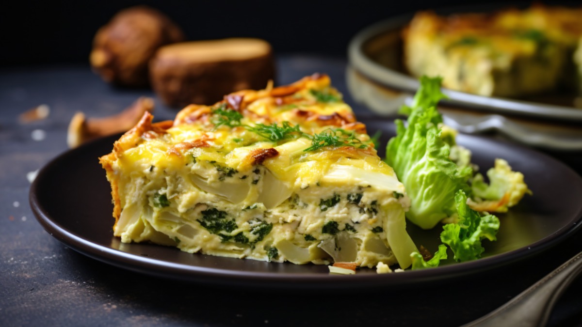 Ein Stück Wirsing-Quiche auf einem Teller. Daneben liegt ein Kohlblatt.