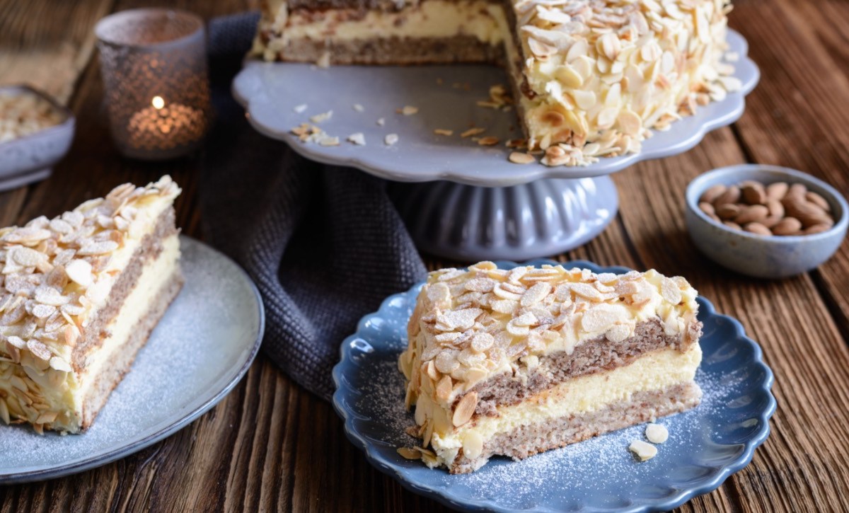 Zwei StÃ¼cke schwedische Mandeltorte auf Tellern im Vordergrund. Dahinter die restliche Torte auf einer Kuchenplatte.