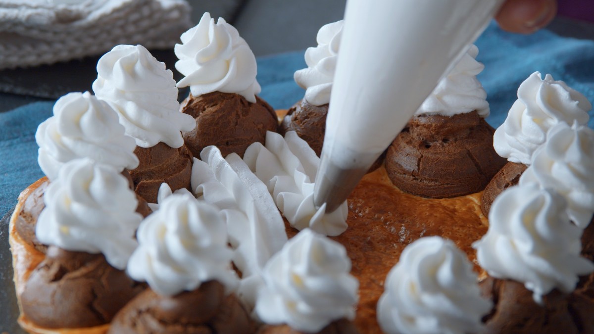 Windbeutel-Blätterteig-Kuchen, auf den Sahne gespritzt wird.