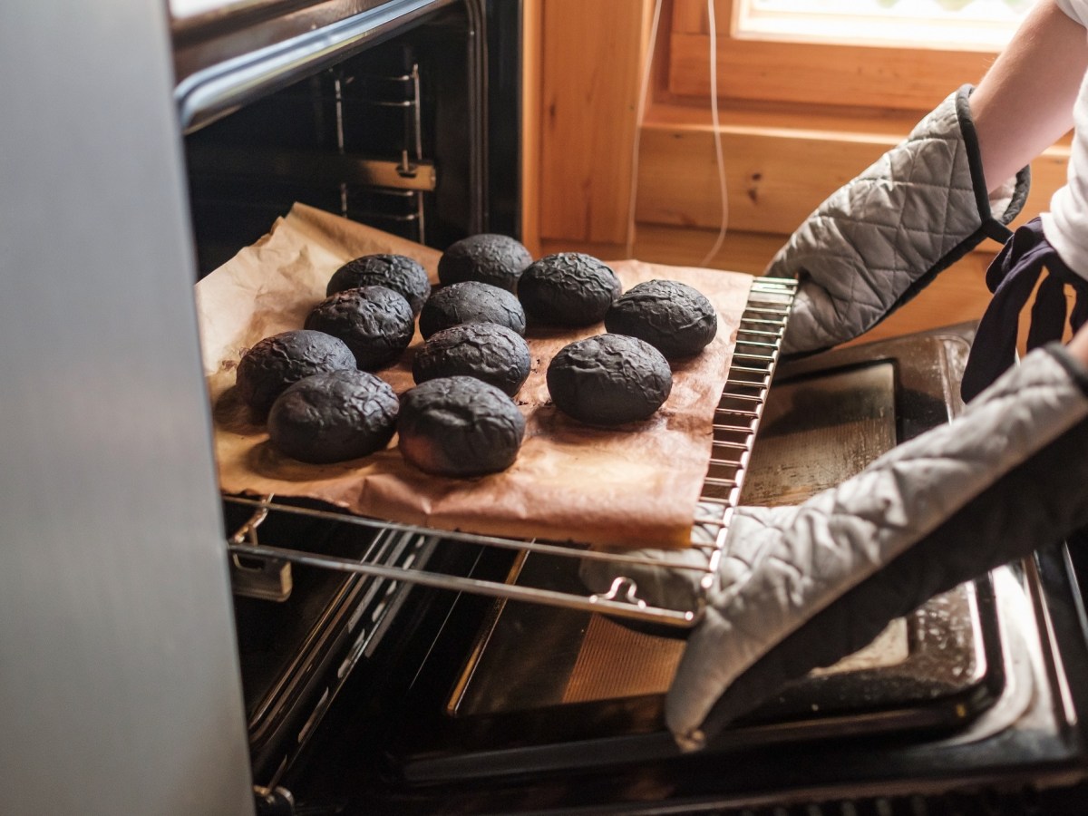 Angebranntes Essen: Eine Person mit Ofenhandschuhen holt verbrannte Brötchen aus einem Ofen.