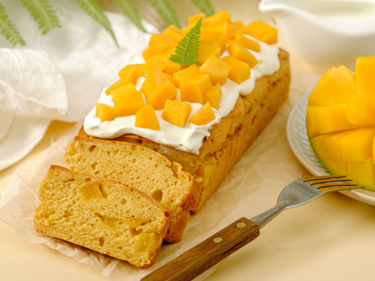 Mango-Kokos-Kuchen aufgeschnitten auf einem Brett. Eine aufgeschnittene Mango steht daneben.