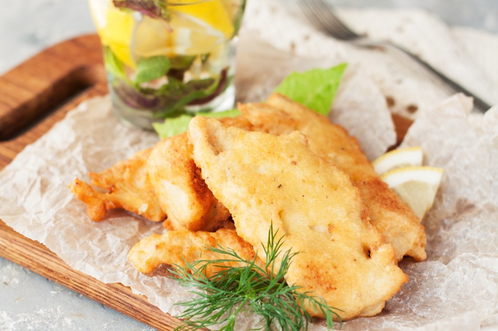 Fisch in Bierteig auf Backpapier mit Kräutern und Zitronenscheiben.