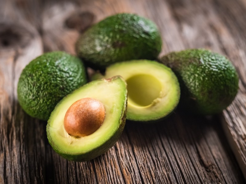 Ist Avocado gesund? Mehrere Avocados liegen auf einem Tisch, davon eine aufgeschnitten