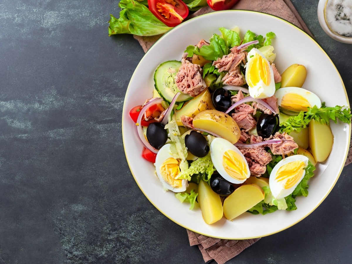 Weißer Teller mit Salade nicoise auf dunklem Untergrund