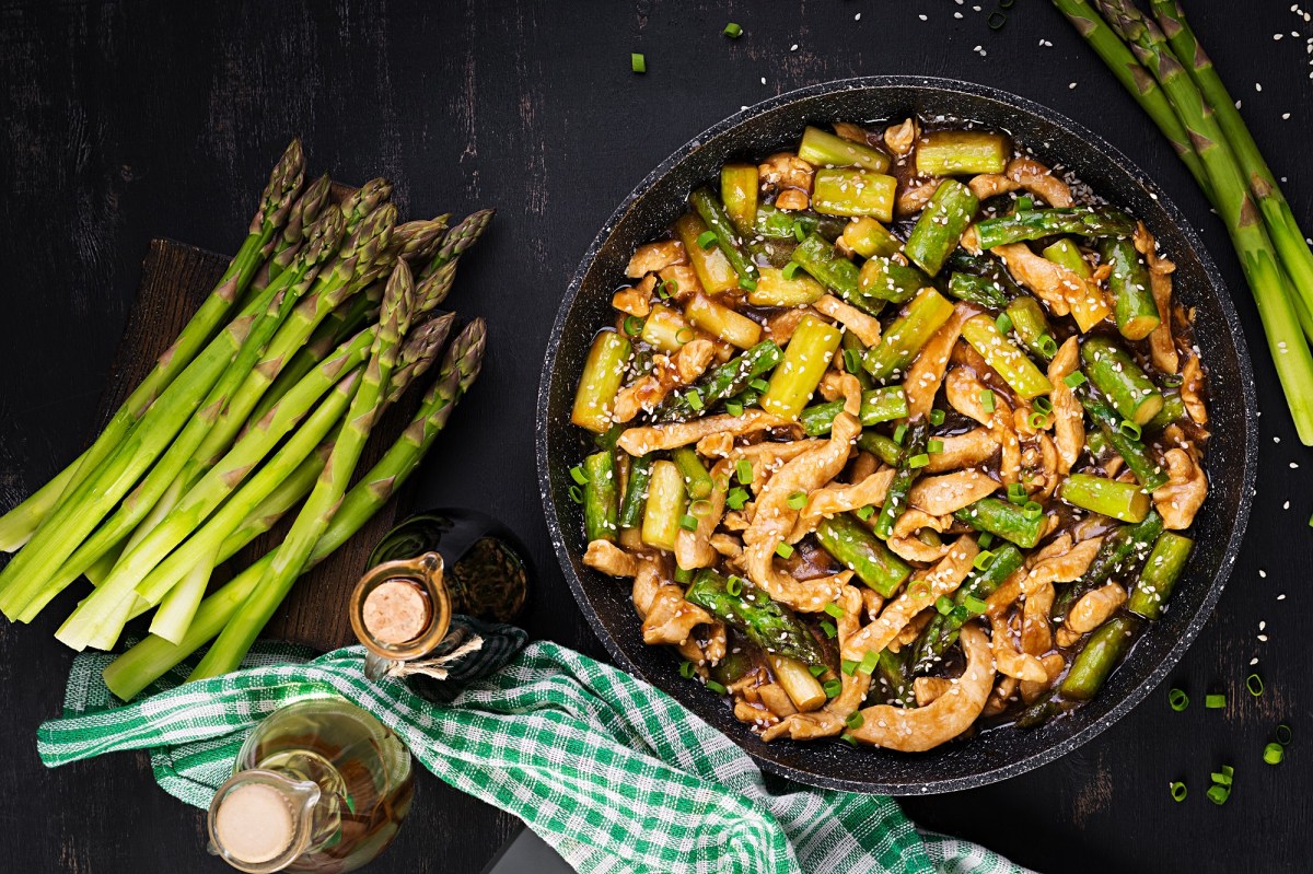 Spargel-Hähnchen-Pfanne, daneben liegen Stangen grüner Spargel und einige Flaschen mit Soja- und Austernsoße