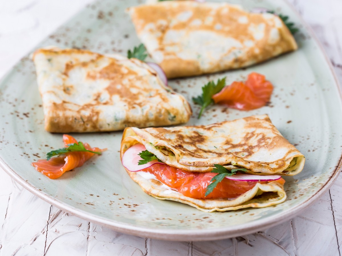 Drei Buchweizen-Pfannkuchen mit Lachs auf einem Teller.