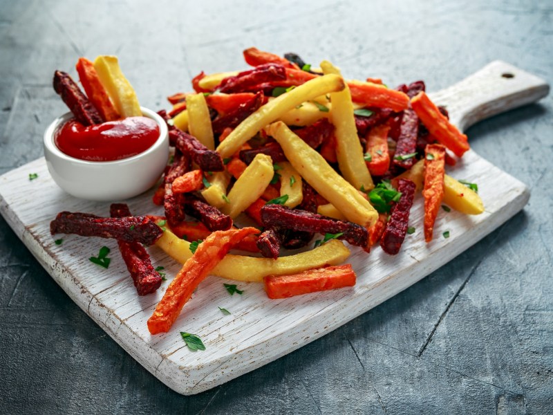 Bunte Ofenpommes auf einem weißen Brettchen mit Ketchup serviert.