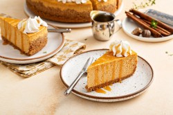 Chai Latte Cheesecake mit Karamellsoße und Sahne auf einem Teller. Im Hintergrund mehr Kuchen und Gewürze.