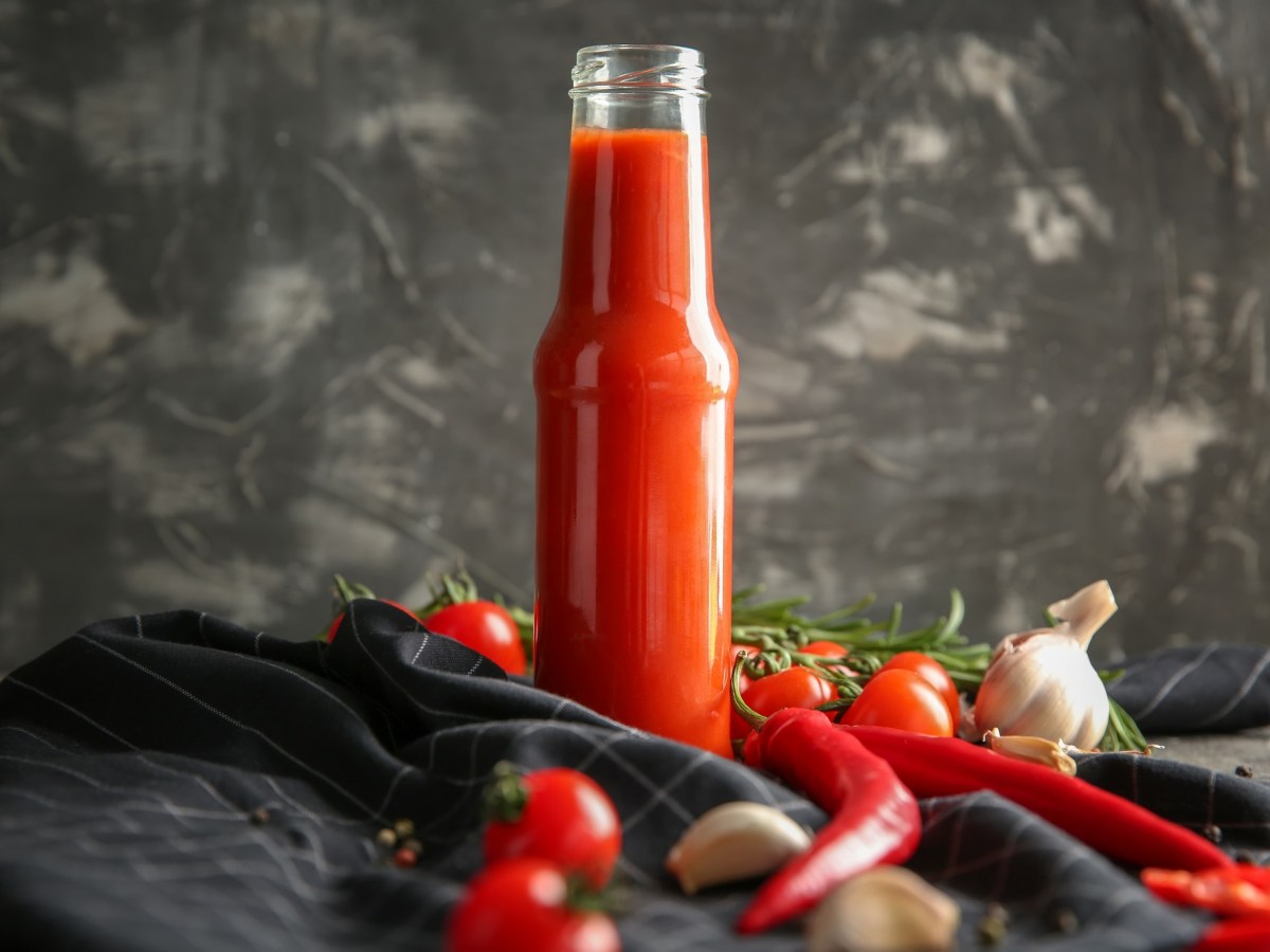 Flasche mit Chilisoße, Chilis, Knoblauch und Tomaten daneben.