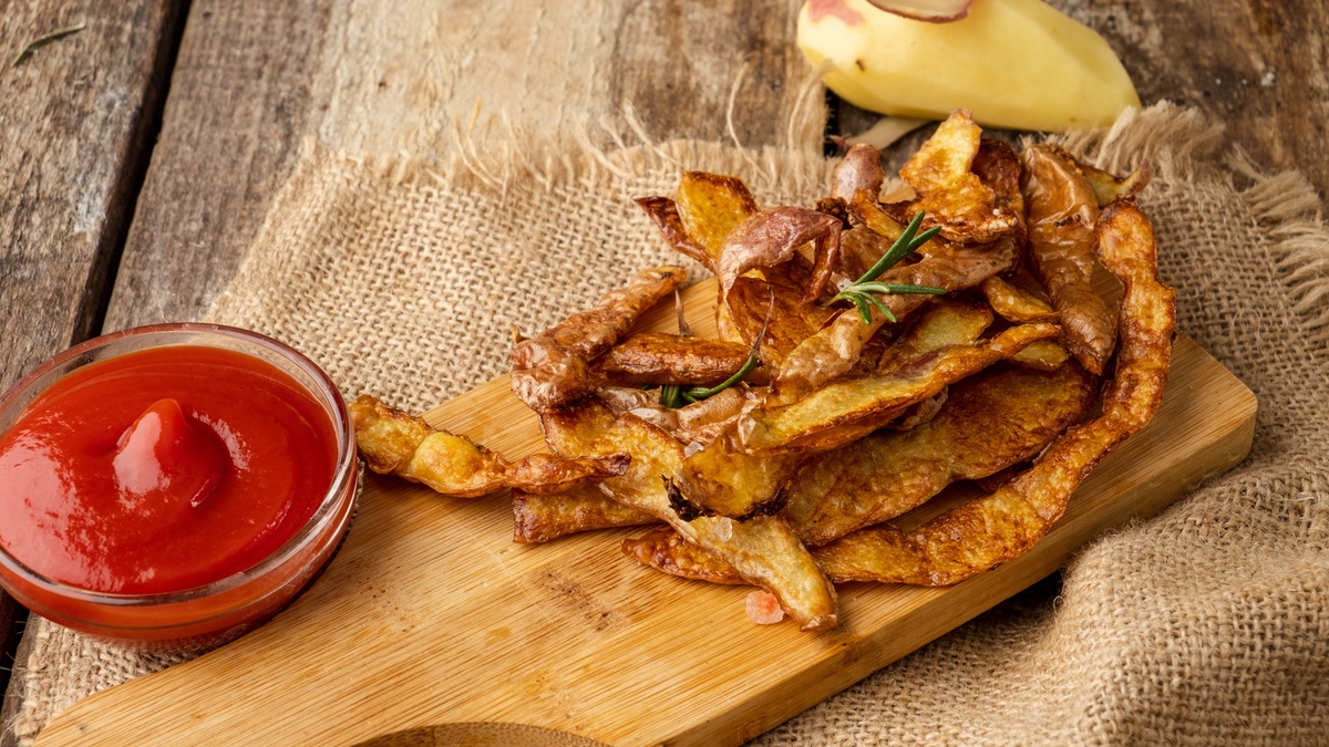 Chips aus Kartoffelschalen auf einem Holzbrett. Daneben eine Schale mit Ketchup.