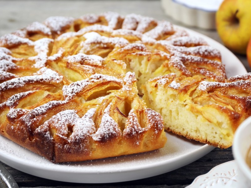 Ein Elsässer Apfelkuchen mit Puderzucker auf einem Teller.