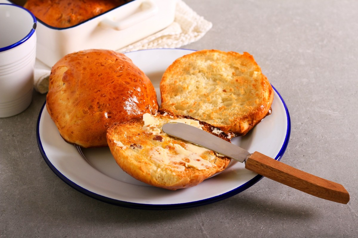 Englische Teekuchen auf einem weißen Teller mit blauem Rand. Sie sind aufgeschnitten und mit Butter bestrichen.