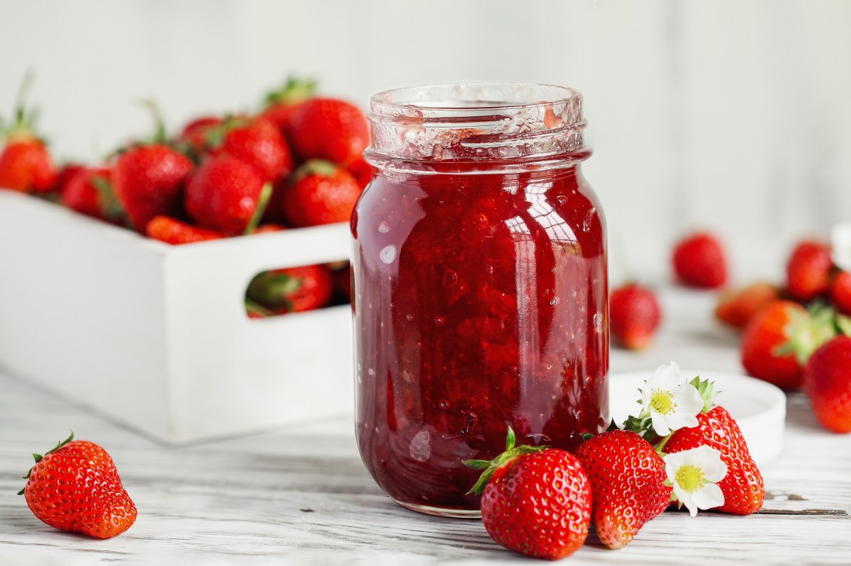 Erdbeermarmelade selber machen: Ein Glas Erdbeermarmelade, daneben und dahinterliegen frische Erdbeeren.