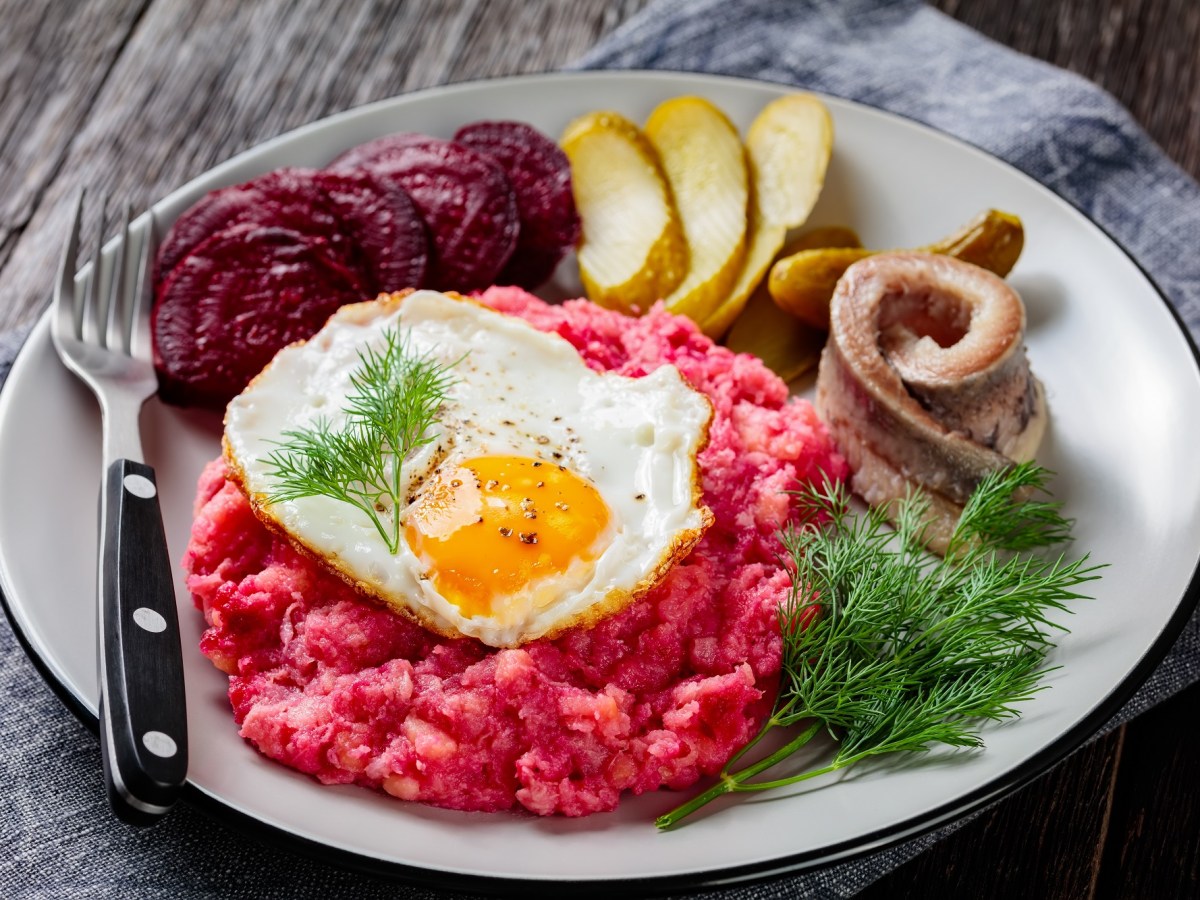 Hamburger Labskaus mit Spiegelei, Rollmops, Roter Bete und Gewürzgurken auf einem Teller, Nahaufnahme.