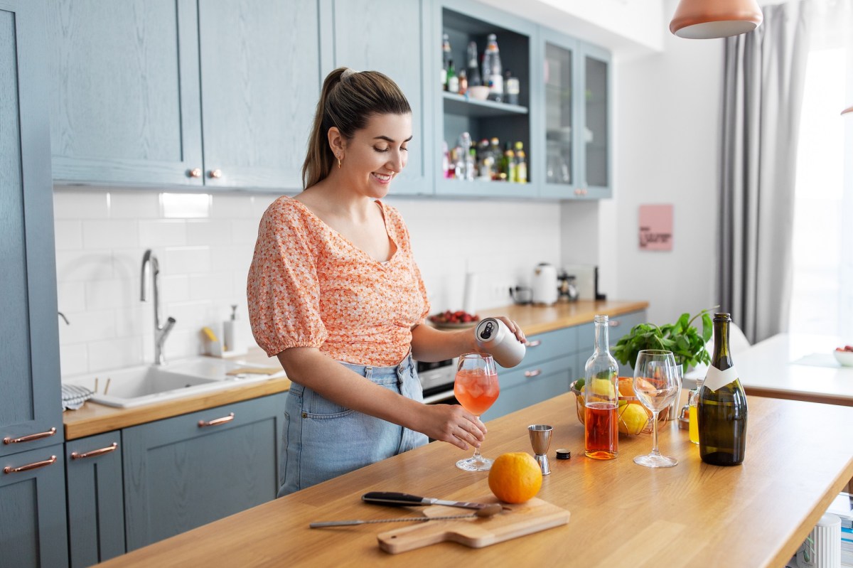 Hausbar-Ausstattung: Eine Frau macht einen Orangen-Cocktail in ihrer Küche