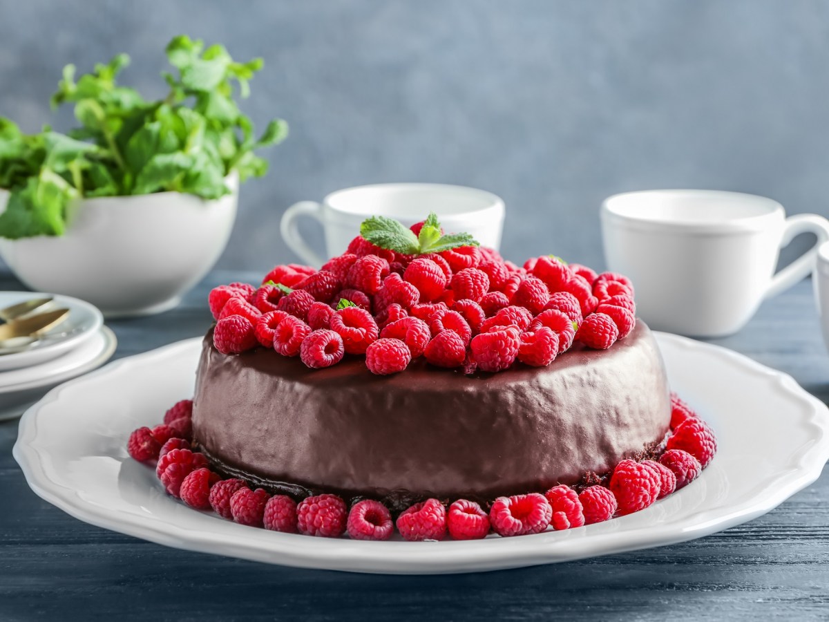 Himbeer-Schokokuchen auf einem weißen Teller. Drum herum liegen frische Himbeeren.