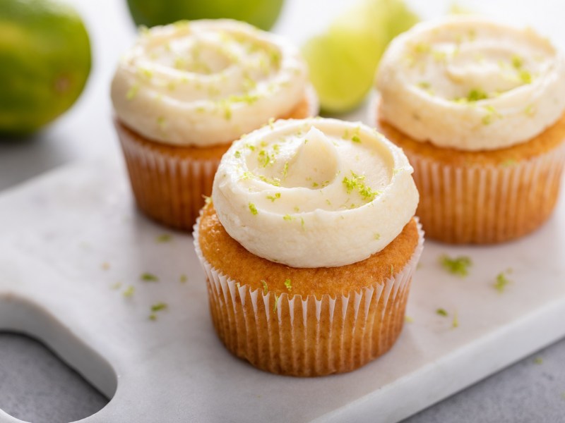 3 Kokos-Limetten-Cupcakes auf einem Brett.