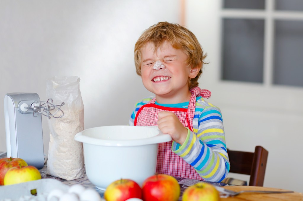 Ein grinsender kleiner Junge beim Backen mit etwas Mehl im Gesicht.