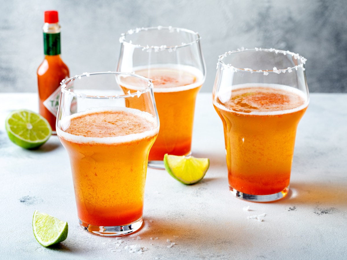 Drei Gläser mit Michelada, Flasche mit Chilisoße und Limettenspalten.