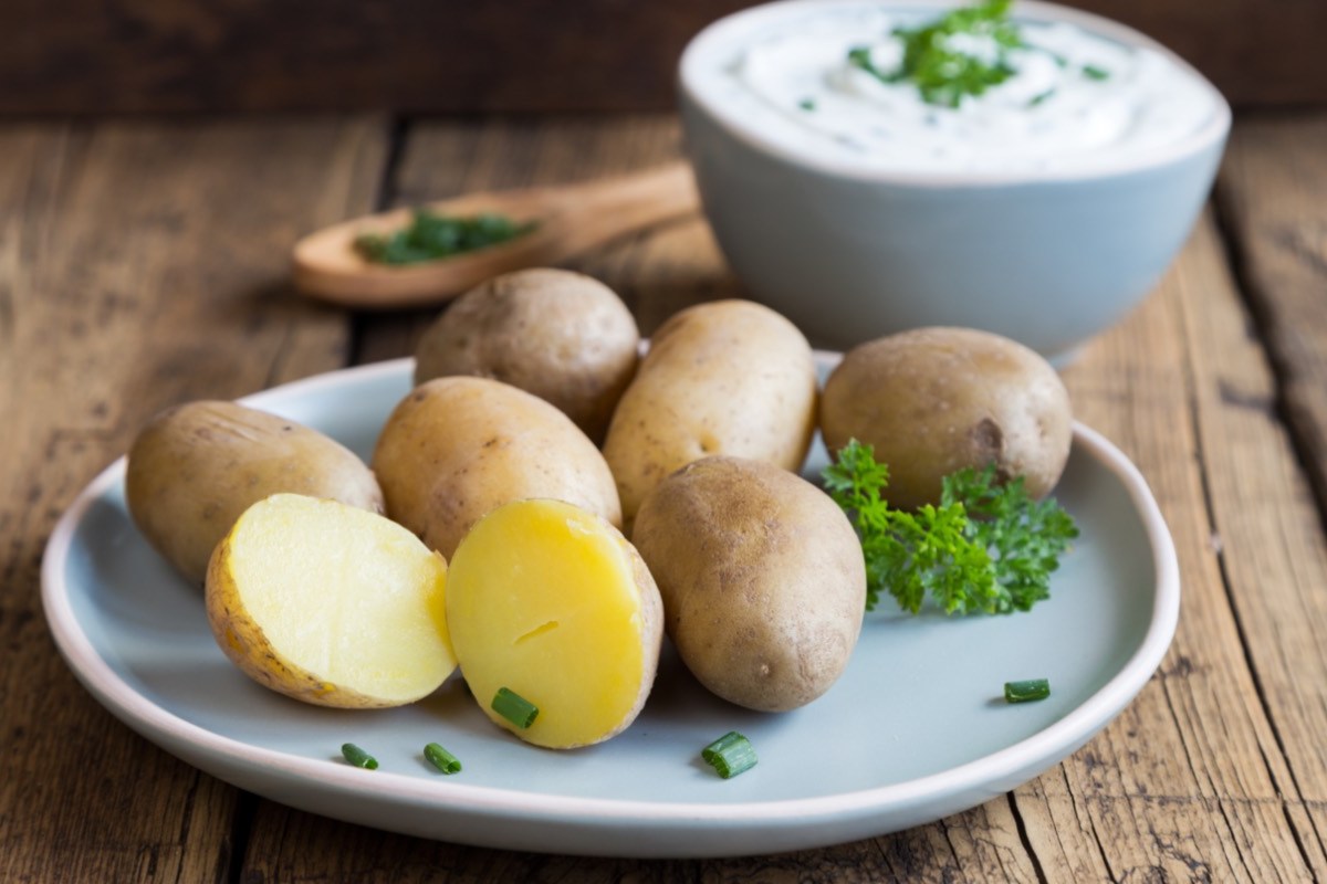 Pellkartoffeln auf einem Teller. Einige sind halbiert. Im Hintergrund steht eine Schüssel mit Kräuterquark.