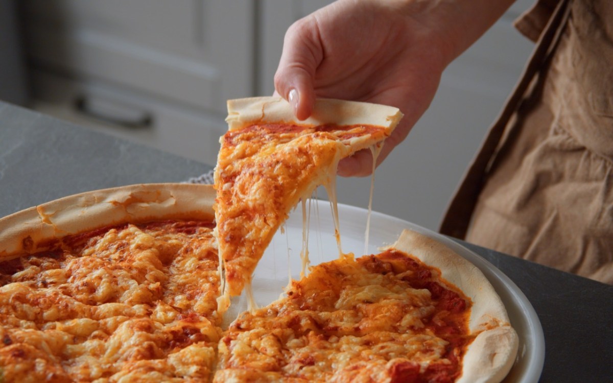 Pizzateig ohne Hefe: Jemand nimmt ein Stück Pizza hoch.