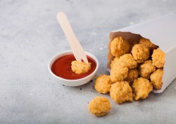 Popcorn Chicken in einer Papiertüte, aus der einige Stücke herauskullern. Daneben Ketchup