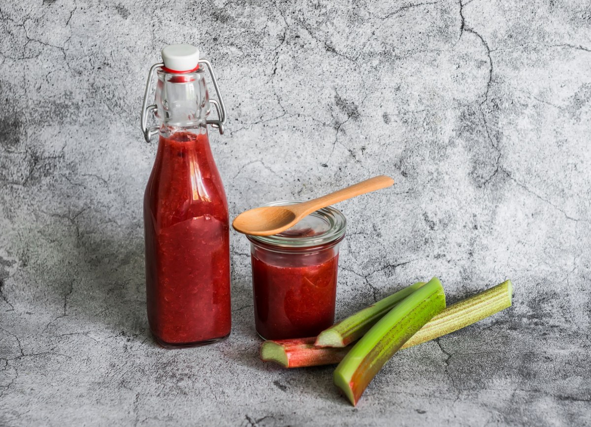 Flasche und Glas mit Rhabarber-Ketchup, Holzlöffel und Rhabarberstangen.