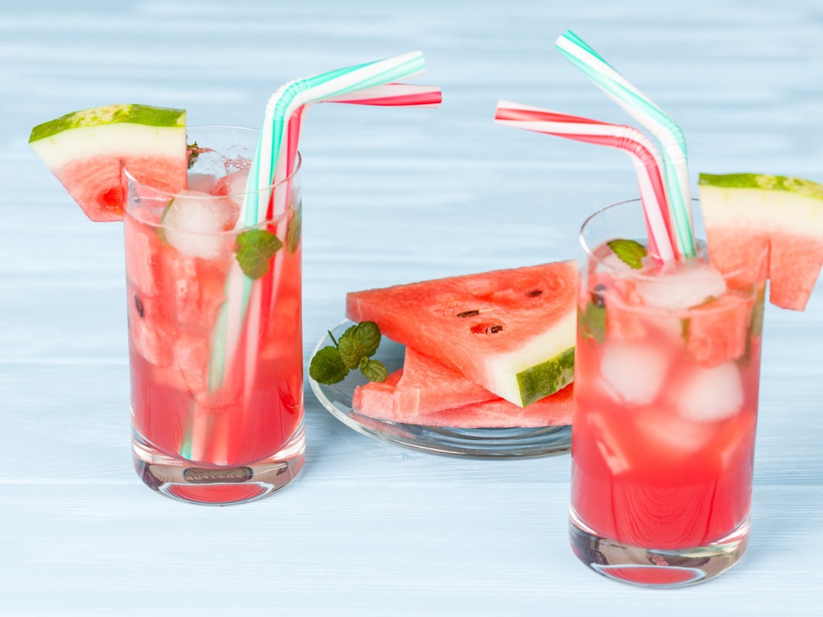2 Gläser Sommerbowle mit Melone, Eiswürfeln und Strohhalmen, dazwischen ein Teller mit Melonenscheiben.