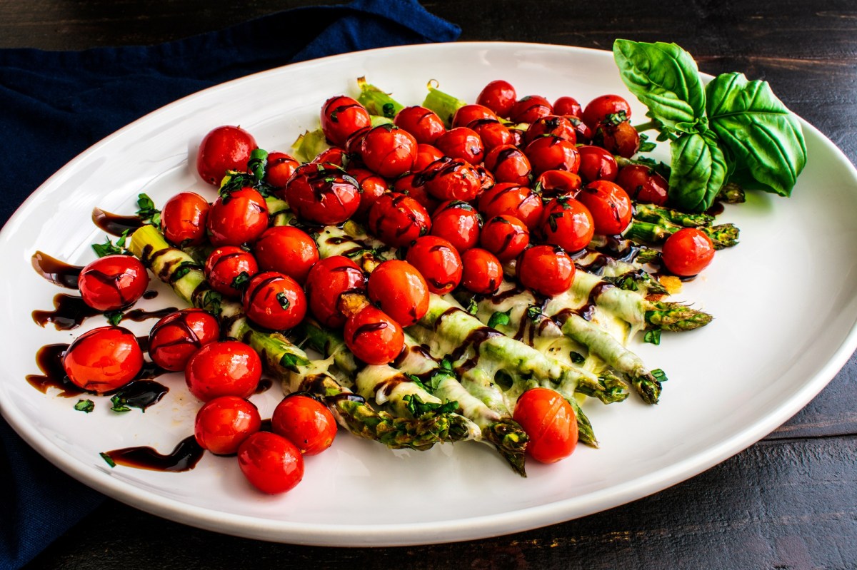 Überbackener Spargel Caprese mit Tomaten und Mozzarella, garniert mit Basilikum und Balsamico.
