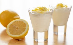 2 Gläser mit Zitronenmousse. Daneben liegt eine halbierte, frische Zitrone.