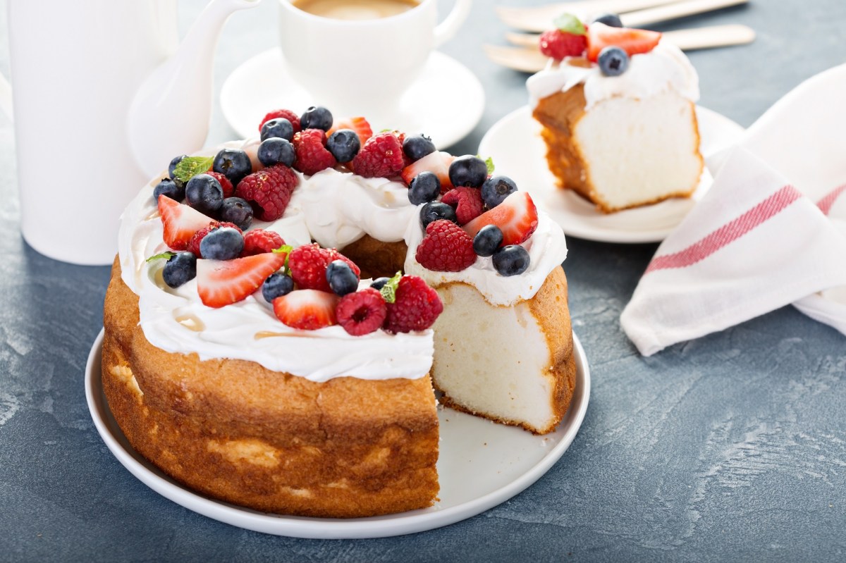 Angel Food Cake, von dem ein Stück angeschnitten wurde, auf einem weißen Teller. Der Kuchen ist garniert mit frischen Beeren.