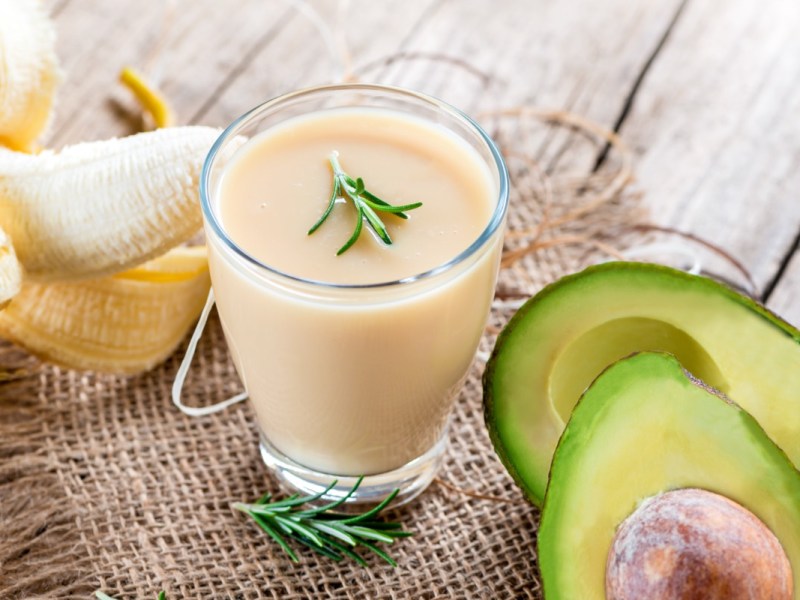 Ein Avocado-Bananen-Smoothie im Glas. Drumherum Zutaten.