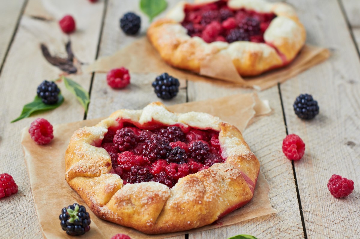 Zwei Beeren-Galettes auf einem Holztisch. Drum herum liegen frische Beeren.