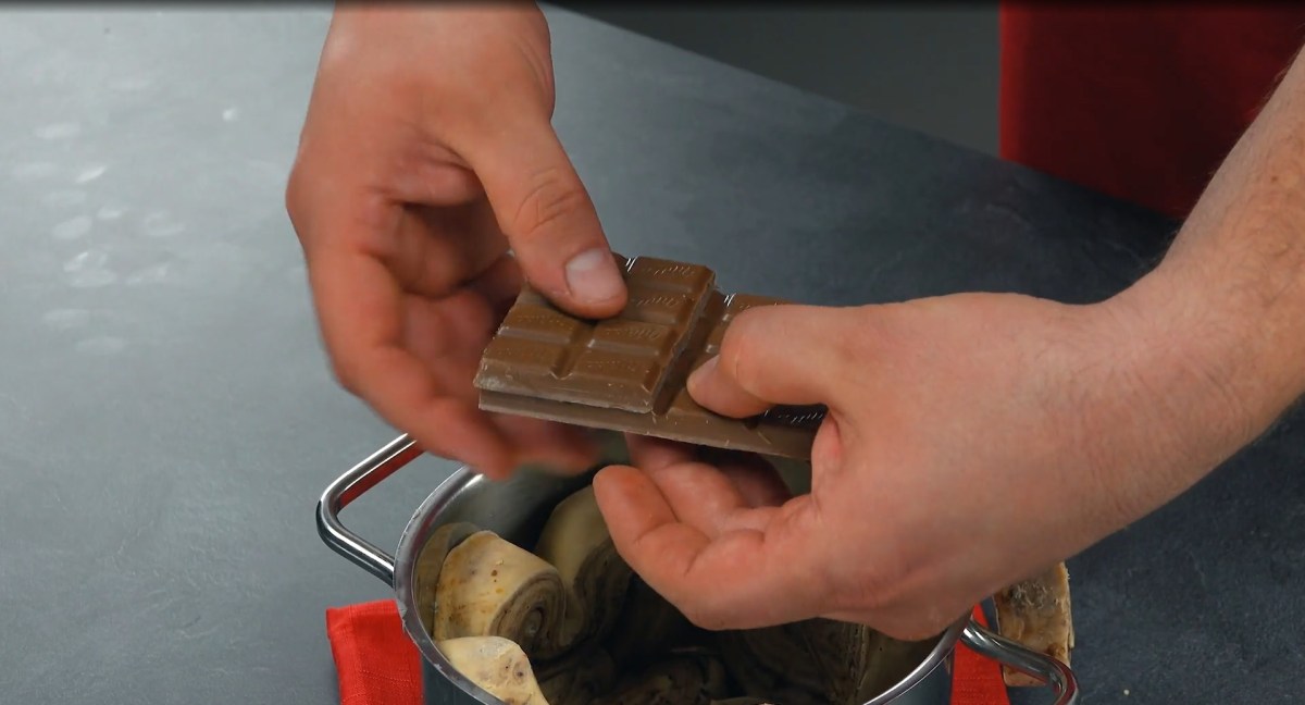 Blätterteigkuchen mit Schokolade aus dem Topf: Teigstücke in einem Topf, über dem zwei Hände eine Tafel Schokolade zerbrechen