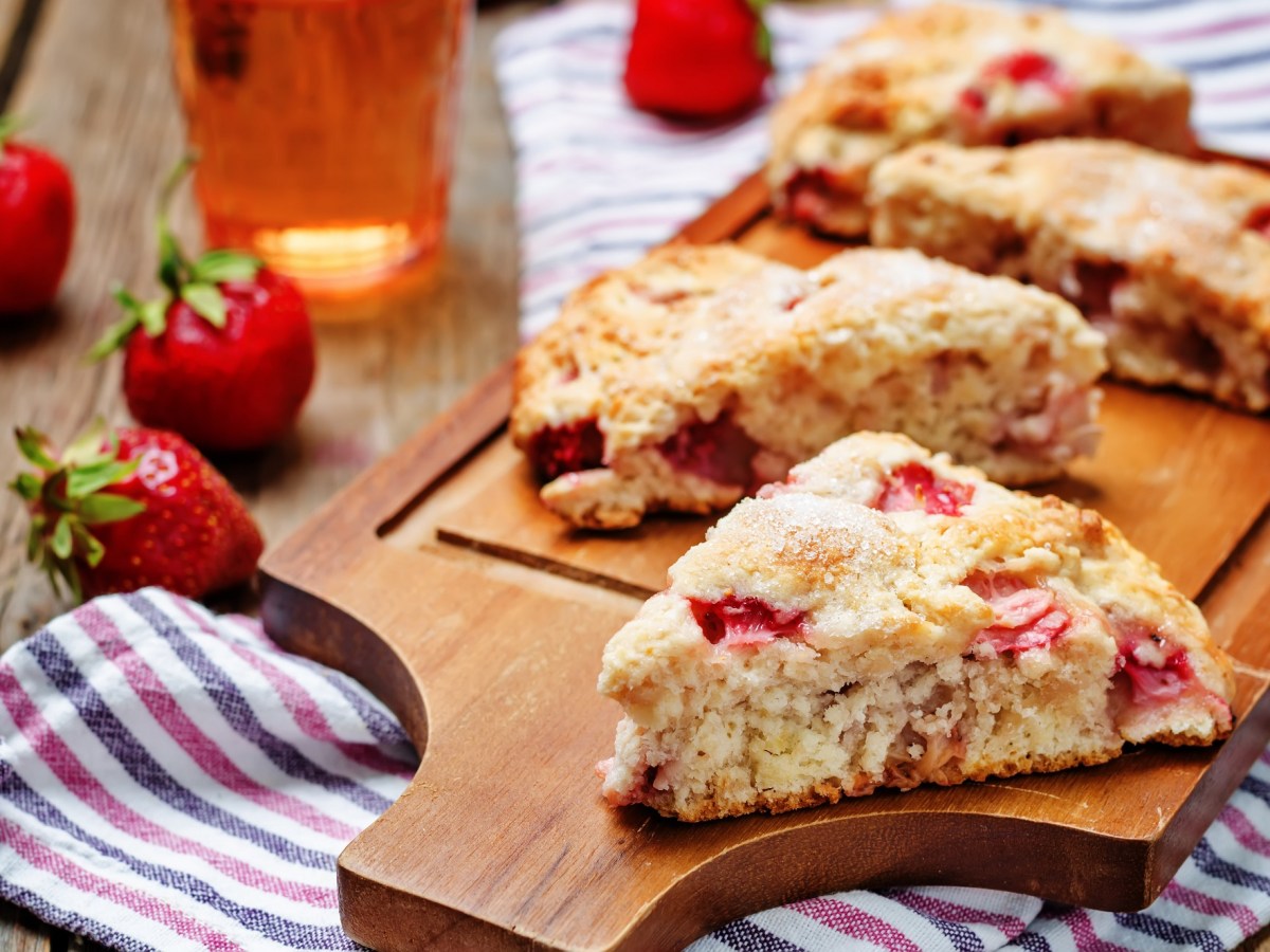 Erdbeer-Buttermilch-Scones auf einem Brett, Erdbeeren und gestreiftes KÃ¼chentuch.