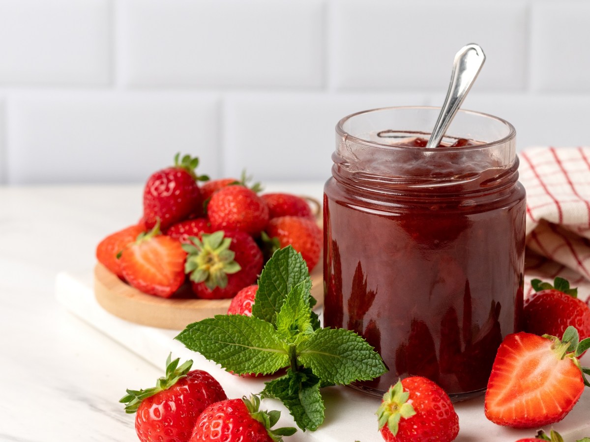 Ein Glas Erdbeer-Kokos-Marmelade mit einem LÃ¶ffel darin, drumherum frische Erdbeeren.