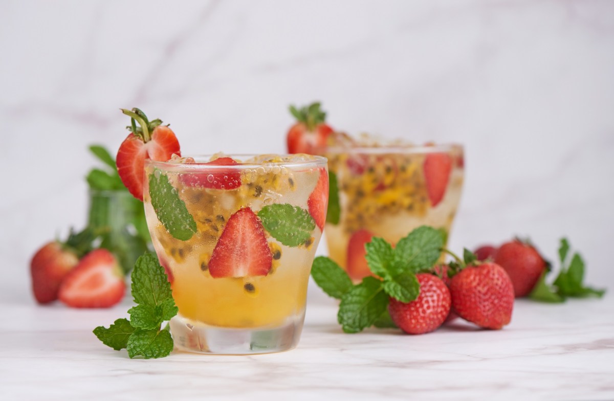 Zwei Gläser Erdbeer-Maracuja-Limonade auf einem Marmor-Tisch. Daneben frische Erdbeeren und Minze.