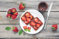 Erdbeer-Nutella-Toasts auf einem weoßen Teller. Daneben stehen ein Glas Nutella und es liegen einige Erdbeeren bereit.